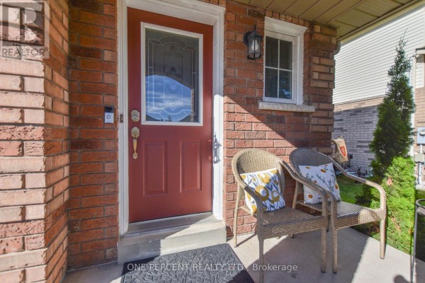 Close-up of the red front door with a window, flanked by brick and a wicker chair. - 90 Breeze Drive, Bradford West Gwillimbury