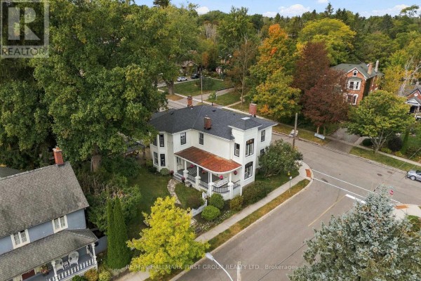 Aerial view of a cream-colored house with a wraparound porch surrounded by trees. - 90 Brown Street, Port Hope