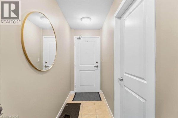 Apartment entryway with beige walls, tiled floor, a white door, and a round gold mirror. - 90 Charlton Avenue W Unit# 203, Hamilton