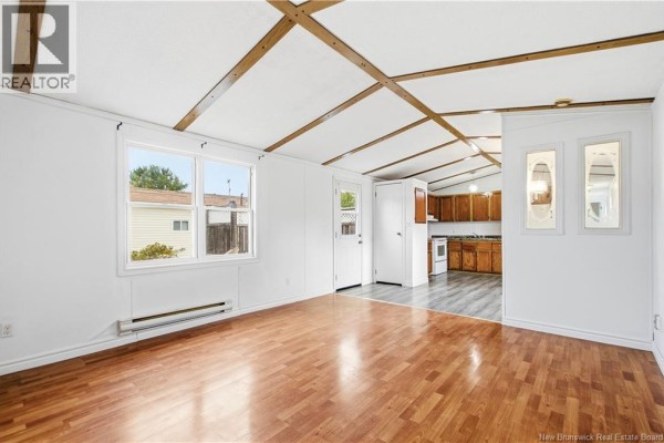 Living area with wood laminate floors, white walls, and view into the kitchen. - 90 Eastwood Street, Fredericton