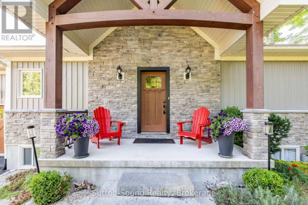 Covered front porch with stone pillars, wood beams, and two red Adirondack chairs. - 90 Graham Crescent, South Bruce Peninsula