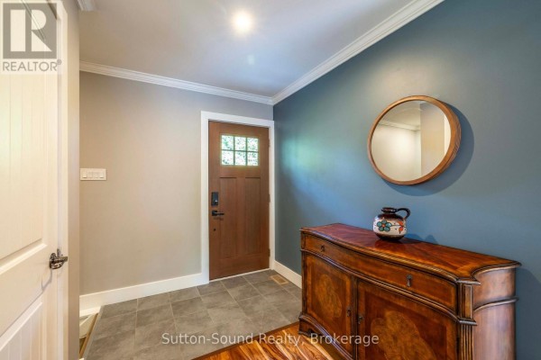Interior entryway with a wooden door, tiled floor, and a round wooden mirror. - 90 Graham Crescent, South Bruce Peninsula