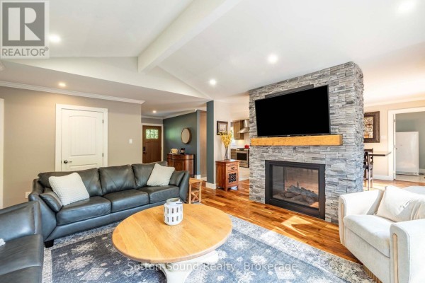 Living room with a stone fireplace, television, leather sofa, and a coffee table. - 90 Graham Crescent, South Bruce Peninsula