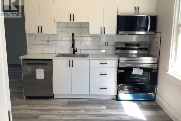 Modern white kitchen with subway tile backsplash, black faucet, stainless steel dishwasher, stove, and microwave. - 90 Kent Street S Unit# 4, Simcoe