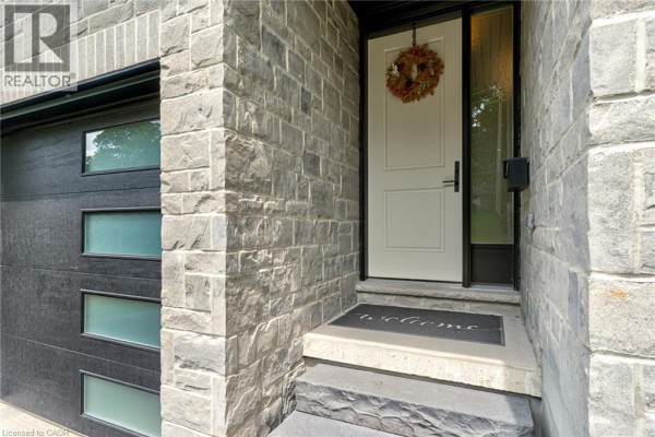 Close-up of the front door and stone wall of a house, with a black garage door visible. - 90 Margaret Avenue N Unit# A, Waterloo