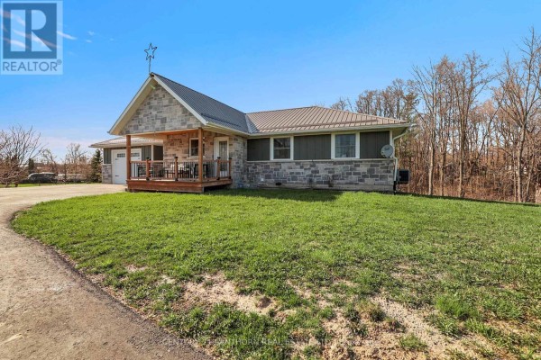 Side view of the house showcasing the lawn, driveway, and rustic exterior. - 90 Seymour Street W, Centre Hastings