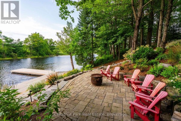 Stone patio with red Adirondack chairs and fire pit overlooking a calm lake. - 90 Swallowdale Road, Huntsville