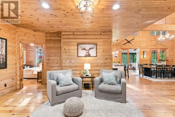 Living room with wood paneling, two armchairs, and open view to dining area - 90 Swallowdale Road Huntsville