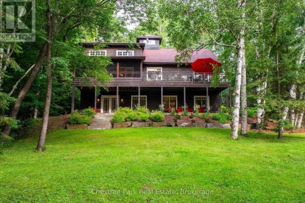 Rear view of a dark wood house with a large deck and green lawn. - 90 Swallowdale Road, Huntsville