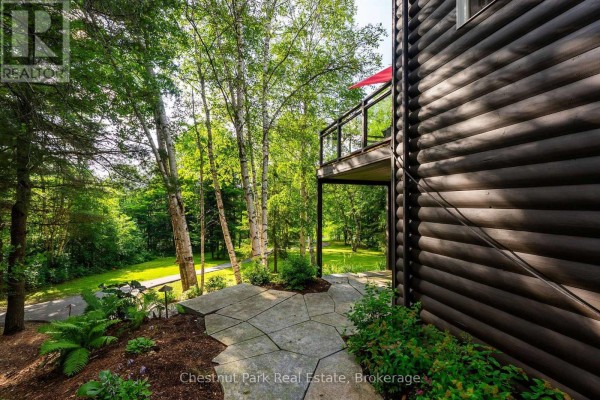 Log cabin exterior with stone path and balcony surrounded by trees - 90 Swallowdale Road Huntsville