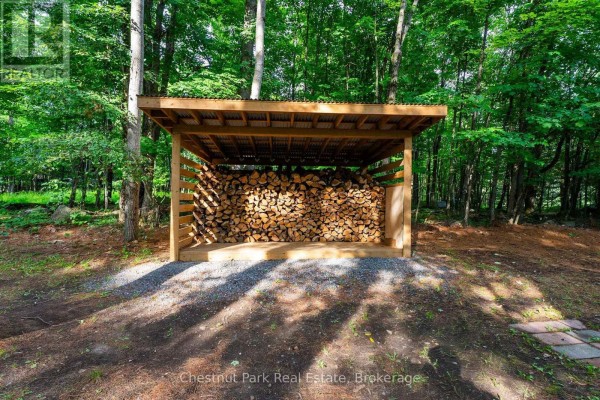 Log shed with stacked firewood in a wooded yard - 90 Swallowdale Road Huntsville