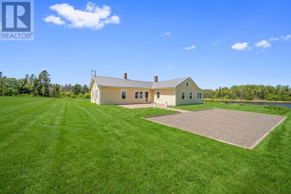 Yellow house with a red-brick chimney sits on a green lawn with water in the distance. - 90 Tuplin Rd, Ellerslie Bideford