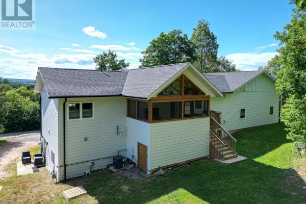 Rear exterior view of white house with screened-in sunroom and wooden deck. - 90 Young Drive, Powassan