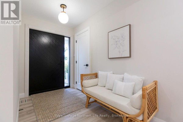 Foyer with black geometric door, light wood floors, and rattan bench. - 90 Young Drive, Powassan