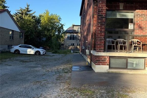 Gravel driveway next to brick building with trees and neighboring houses. - 900 Kennedy Road, Scarborough