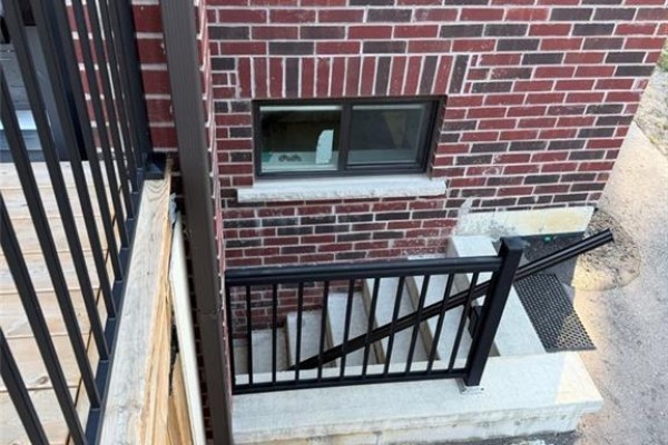 Exterior brick wall with a small window above concrete steps and black metal railings. - 900 Kennedy Road, Scarborough