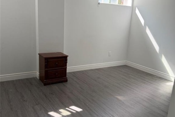 Bedroom with light grey walls, dark grey laminate flooring, and a wooden nightstand. - 900 Kennedy Road, Scarborough