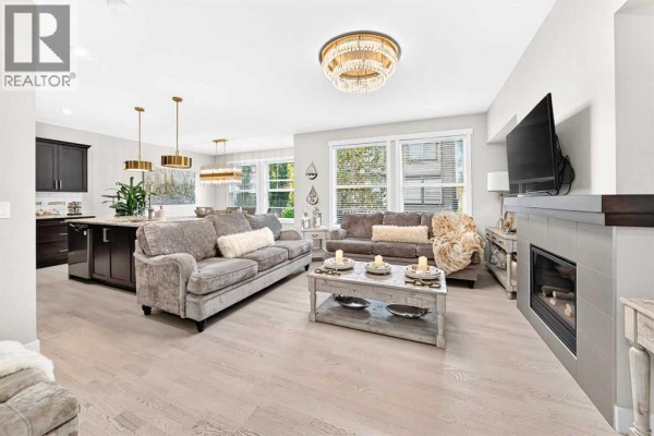 Open-concept living and dining area with modern furniture, a fireplace, and kitchen island. - 901, 110 Coopers Common Sw, Airdrie