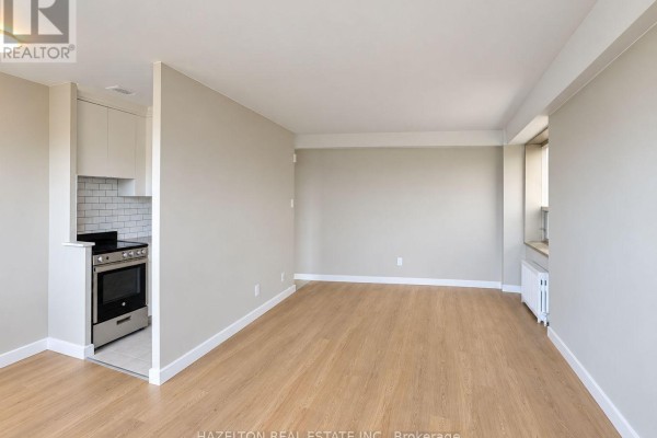 Empty living room with beige walls, light wood floors, and a large window. - 901 - 206 St George Street, Toronto