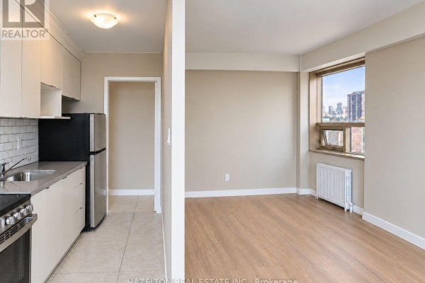 Kitchen with stainless steel appliances and a beige living area with a window view. - 901 - 206 St George Street, Toronto