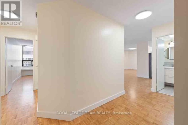 Interior hallway with beige walls, a hardwood floor, and a doorway to a bathroom. - 901 - 40 Arthur Street, Ottawa