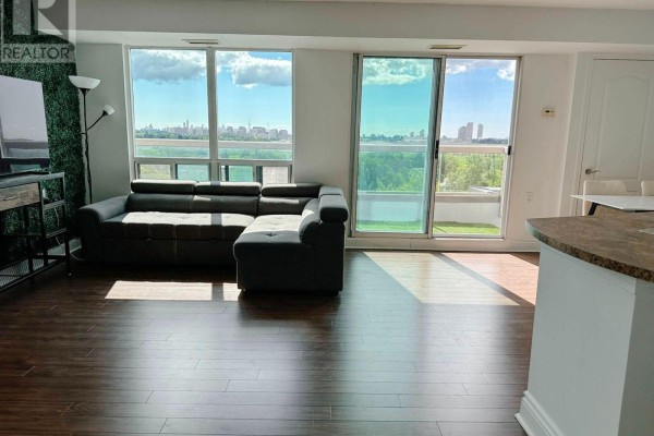 Living room with large windows offering city and tree views, and a sectional sofa. - 901 - 935 Sheppard Avenue W, Toronto