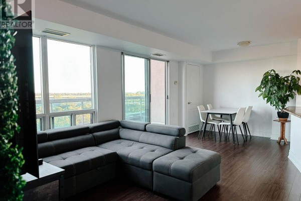Living and dining area with a grey sectional sofa, white dining set, and large windows. - 901 - 935 Sheppard Avenue W, Toronto