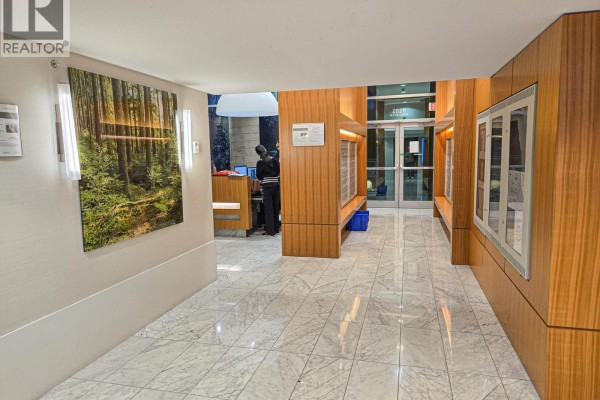 Building lobby with marble floors, wood paneling, artwork, and reception desk. - 901 8131 Nunavut Lane, Vancouver