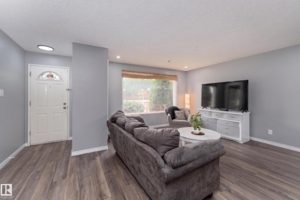 Living room showing sofa, brick feature wall with fireplace, and view into kitchen and dining area. - 9012 Meadowlark Rd Nw, Edmonton