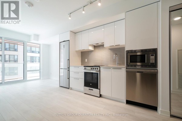 Apartment kitchen with white cabinets, stainless steel appliances, grey tiled backsplash, and light wood floors. - 902 - 18 Maitland Terrace, Toronto
