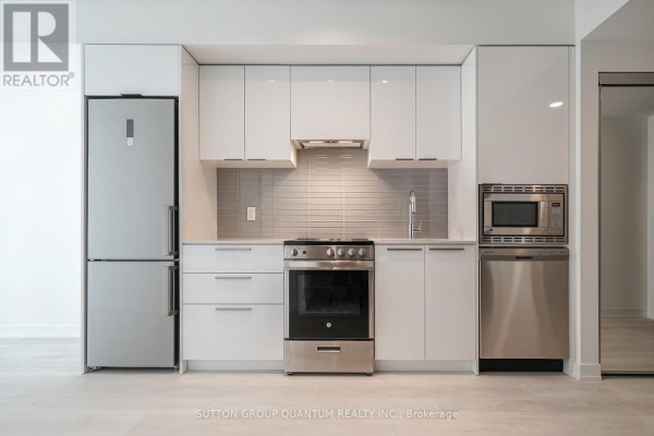 Apartment kitchen with white cabinets, stainless steel appliances, grey tiled backsplash, and light wood floors. - 902 - 18 Maitland Terrace, Toronto
