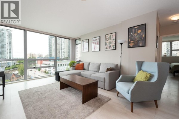 Living room with a sofa, armchair, coffee table, and a view of the city through large windows. - 902 14 Begbie Street, New Westminster