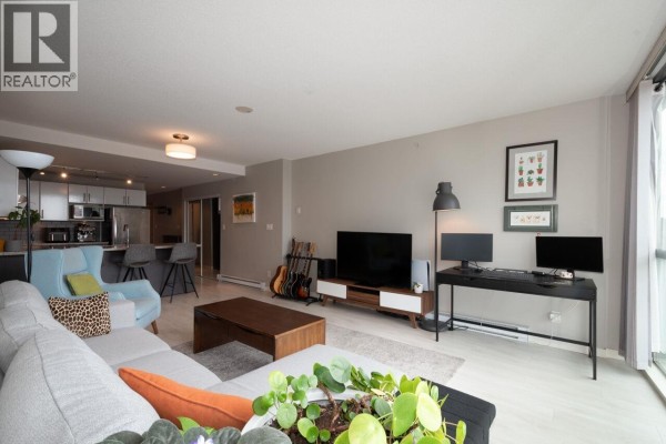 Living room showing the entertainment unit, desk, sofa, and kitchen island with bar stools. - 902 14 Begbie Street, New Westminster