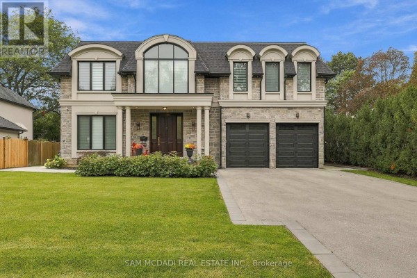 A two-story residential house with a stone facade, arched windows, and a double garage under a blue sky. - 902 Parkland Avenue, Mississauga