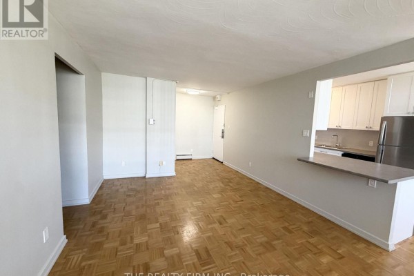Living room with light gray walls, a parquet floor, and an open doorway to a kitchen. - 903 - 1209 Richmond Street, London East