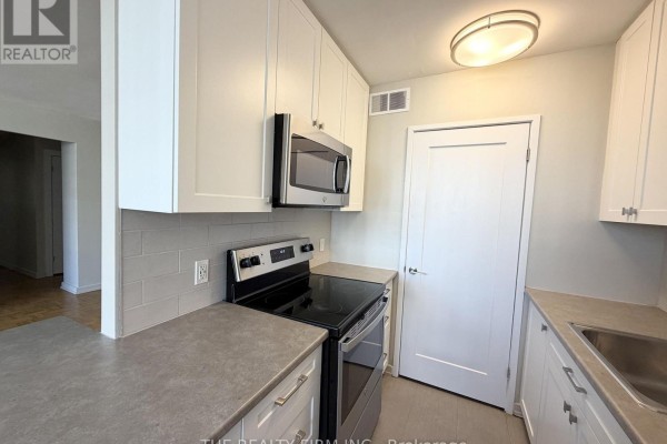 Close-up of a kitchen with white cabinets, stainless steel appliances, and gray countertops. - 903 - 1209 Richmond Street, London East