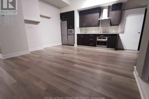 Open-concept living area with light wood laminate flooring and a modern kitchen with dark cabinets and stainless steel appliances. - #903 - 75 The Donway W, Toronto