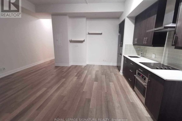 Interior view of the apartment showing the living area and kitchen, with wood laminate flooring and dark cabinetry. - #903 - 75 The Donway W, Toronto
