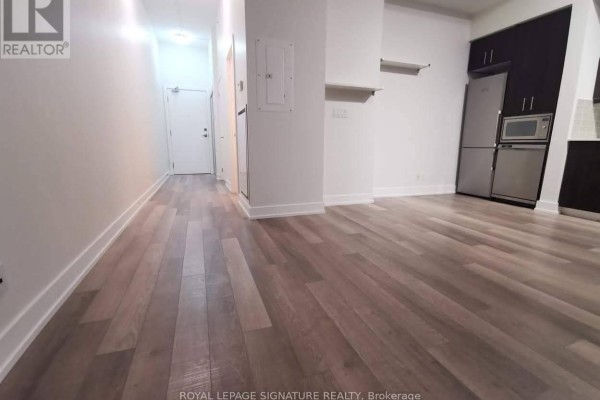 Hallway leading into the living area, with light wood laminate flooring, white walls, and a door on the left. - #903 - 75 The Donway W, Toronto