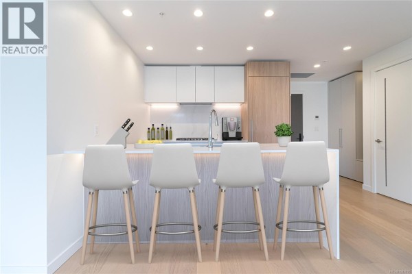 Kitchen with white cabinetry, stainless steel appliances, and a breakfast bar with four stools. - 903 2000 Hannington Rd, Langford