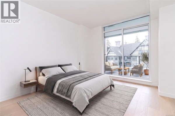 Bedroom with a queen-size bed, wood-frame nightstand, and sliding glass doors to a balcony. - 903 2000 Hannington Rd, Langford