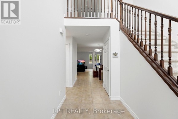 Interior foyer with a view down a hallway towards a living area, and a carpeted staircase on the right. - 903 Bradshaw Crescent, London North