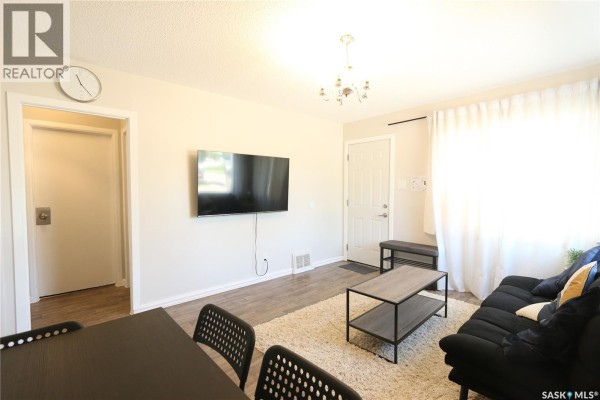Living area with a black sofa, coffee table, and small dining table with chairs. - 903 Robinson Street, Regina