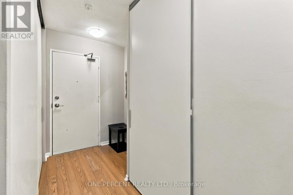 Apartment entrance with a white door, wood-look floor, and a black stool. - 904 - 15 Elizabeth Street N, Mississauga