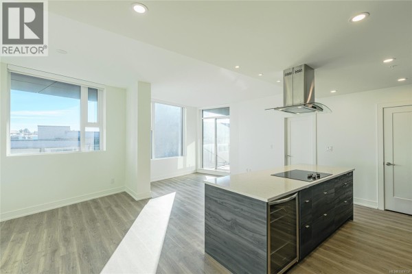 Open concept living area with a kitchen island and natural light from balcony doors. - 904 1628 Store St, Victoria