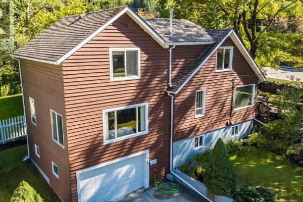 Side view of a two-story house with brown siding, multiple windows, and a concrete driveway. - 904 Fifth Street, Nelson
