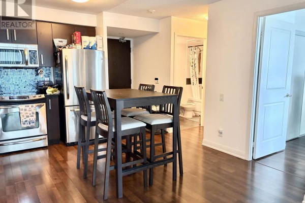 Kitchen area with stainless steel refrigerator, dark cabinets, and a high-top dining table. - 905 - 17 Anndale Drive, Toronto