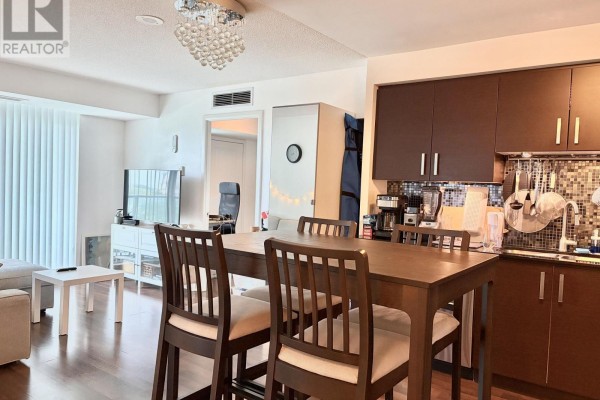View of a dining table with chairs, dark kitchen cabinets, and a living area with a TV. - 905 - 17 Anndale Drive, Toronto