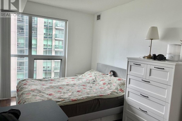 Bedroom with a queen-size bed, floral bedding, white dresser, and large window. - 905 - 17 Anndale Drive, Toronto