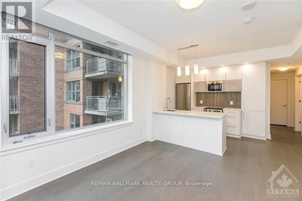 View of the modern kitchen with light wood cabinets, white countertops, and city views from the living area. - 905 - 255 Bay Street, Ottawa